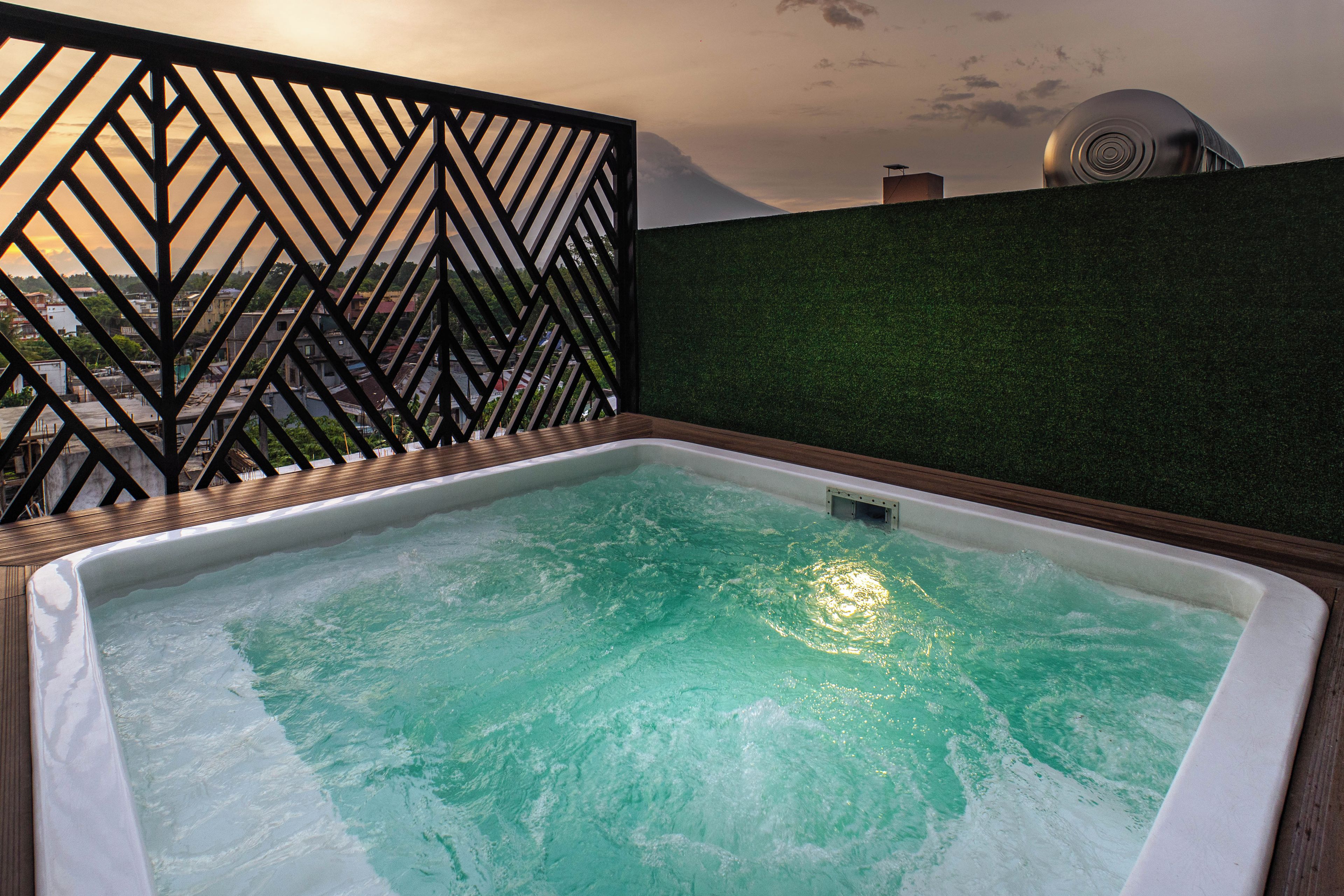 A hot tub with a view of a cityscape through a geometric metal fence.