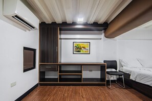 A hotel room with a wooden floor, a bed, a chair, a TV, and a painting on the wall.