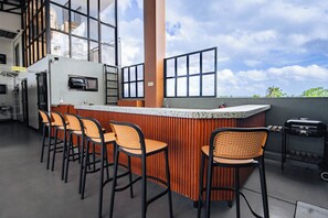 Zona de bar con mostrador, taburetes y parrilla.
