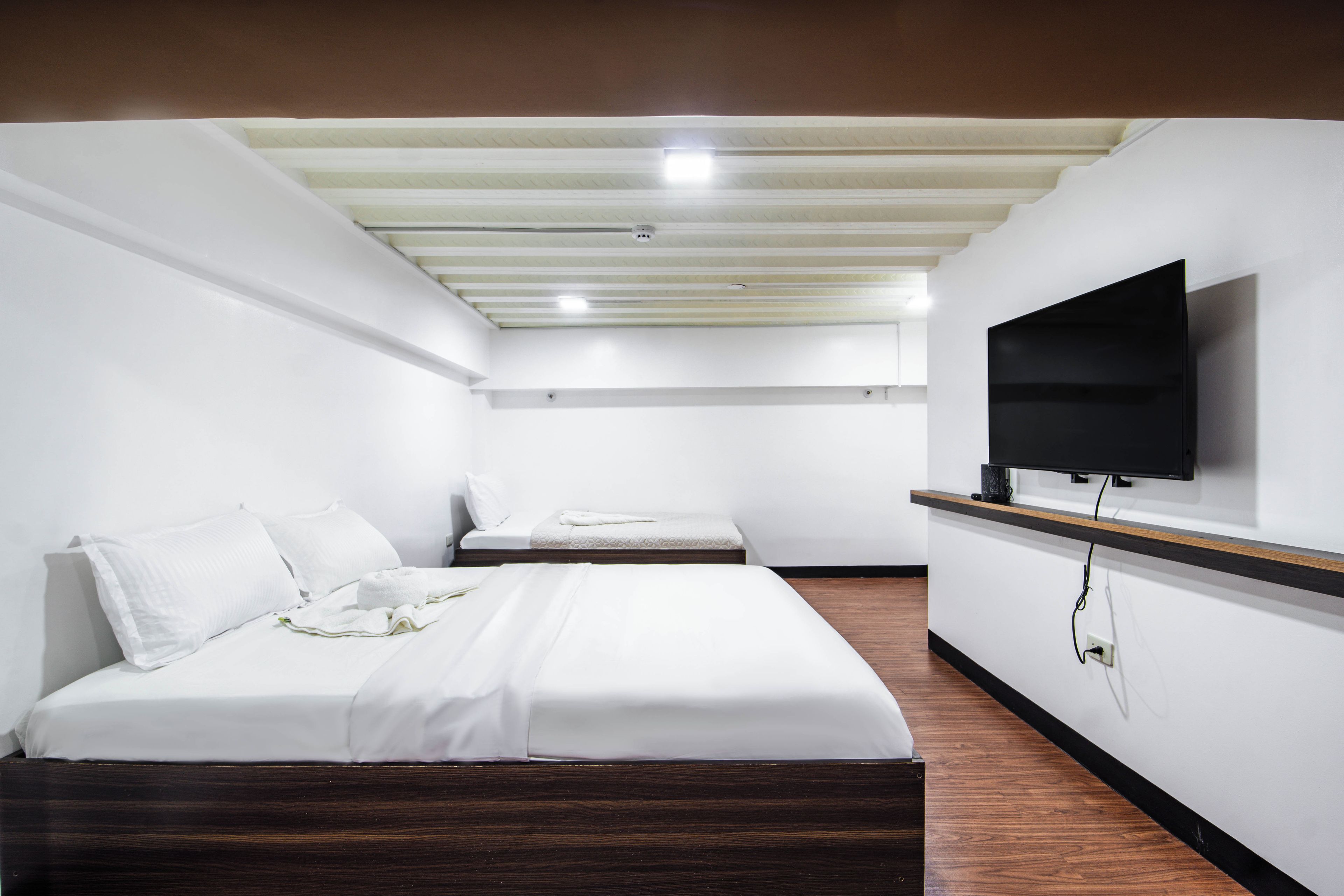 A hotel room with a bed, a TV mounted on the wall, and a wooden floor.