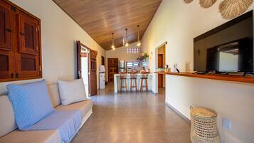 A modern kitchen with a central island, wooden cabinets, and a large TV.