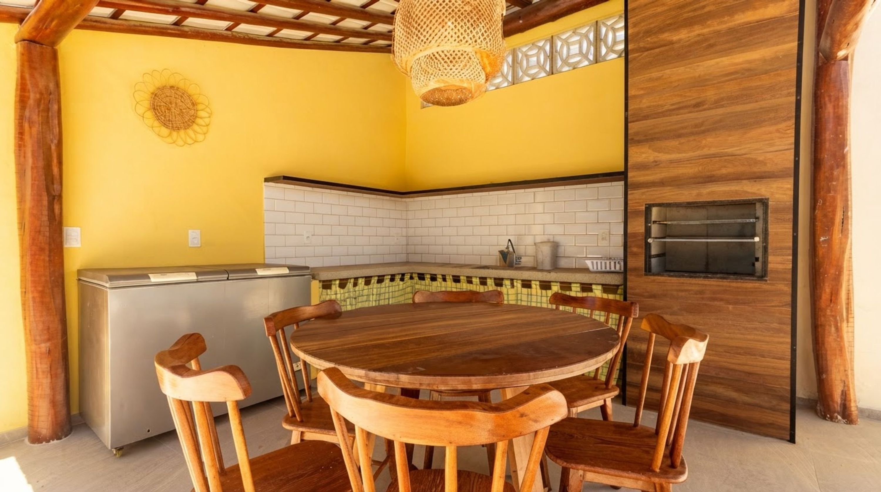 A kitchen with a round wooden table and chairs, a refrigerator, and a pizza oven.
