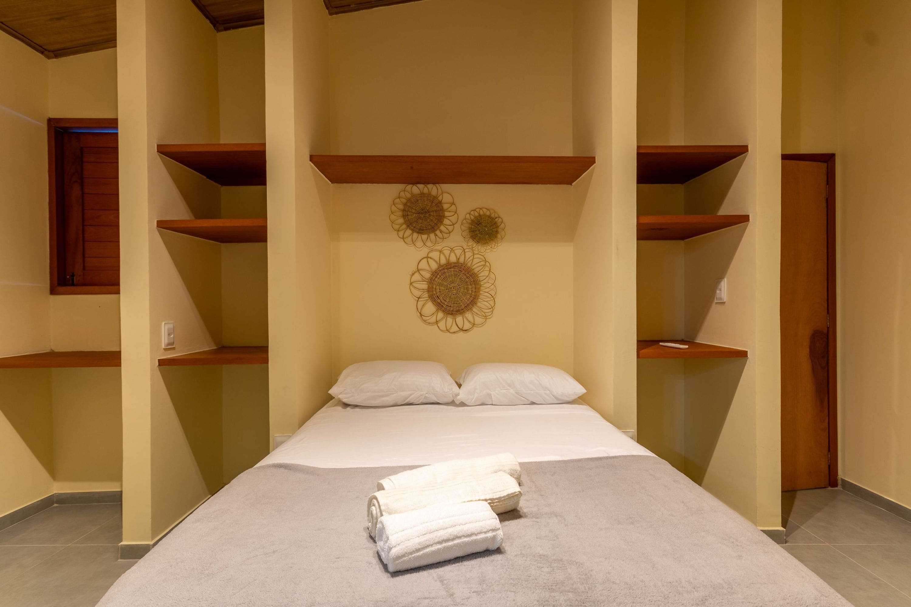 A bedroom with a bed, two pillows, a rolled-up towel, and decorative wall art.