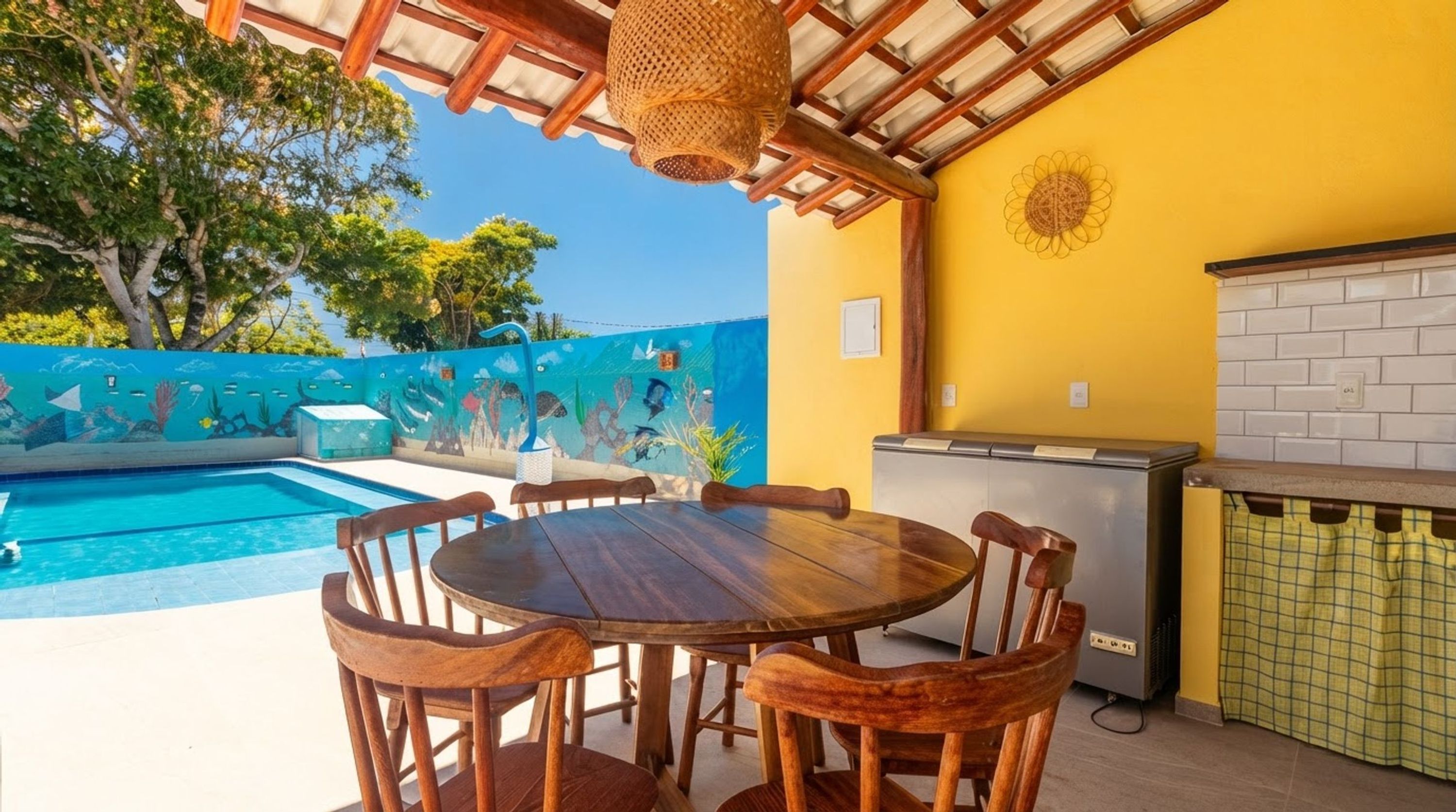 Un área junto a la piscina con mesa y sillas de madera, un refrigerador y un salpicadero de azulejos.