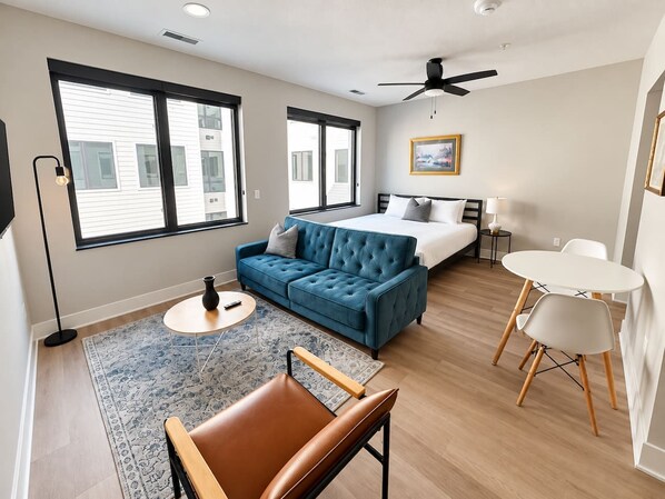 Una habitación de hotel moderna con una cama, un sofá azul, una mesa de comedor y un ventilador de techo.