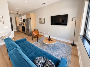 Una sala de estar moderna con un sofá azul, una mesa de centro y un televisor montado en la pared.