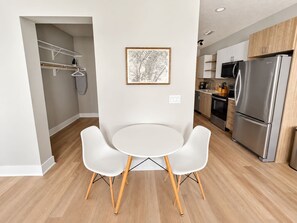 Eine moderne Küche mit einem Edelstahl-Kühlschrank, Holzschränken und einem weißen Esstisch mit zwei Stühlen.