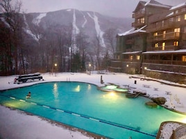 Una piscina con vistas a una cadena montañosa, rodeada por un edificio con varios balcones.
