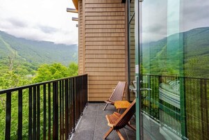 Un balcón con vistas a un paisaje montañoso, dos sillas de madera y un vidrio.