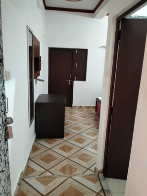 A room with a tiled floor, a dark-colored cabinet, a door, and a wall-mounted light fixture. - DeepYogaRetreat Hotel Deshraj Rishikesh  (rishikesh)