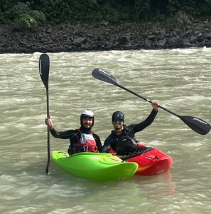 Duas pessoas praticando caiaque em um rio, com uma margem rochosa ao fundo.