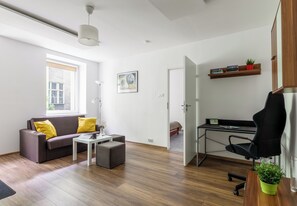A modern living room with a sofa, coffee table, and a desk area with a computer and books. - Piłsudskiego City Center Apartment (Szczecin)