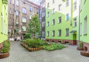 A courtyard with a central tree surrounded by planters, flanked by buildings with multiple windows and balconies. - Piłsudskiego City Center Apartment (Szczecin)