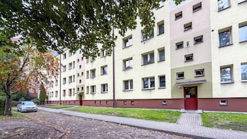 Un edificio residencial de varios pisos con una puerta roja, número 12, y un camino pavimentado cubierto de hojas caídas.