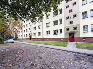 Un edificio residencial de varios pisos con una puerta roja, número 12, y un camino pavimentado cubierto de hojas caídas.