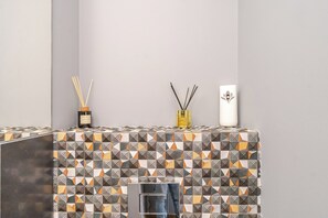 Un baño con salpicadero de azulejos, un espejo y dos recipientes decorativos en un estante.