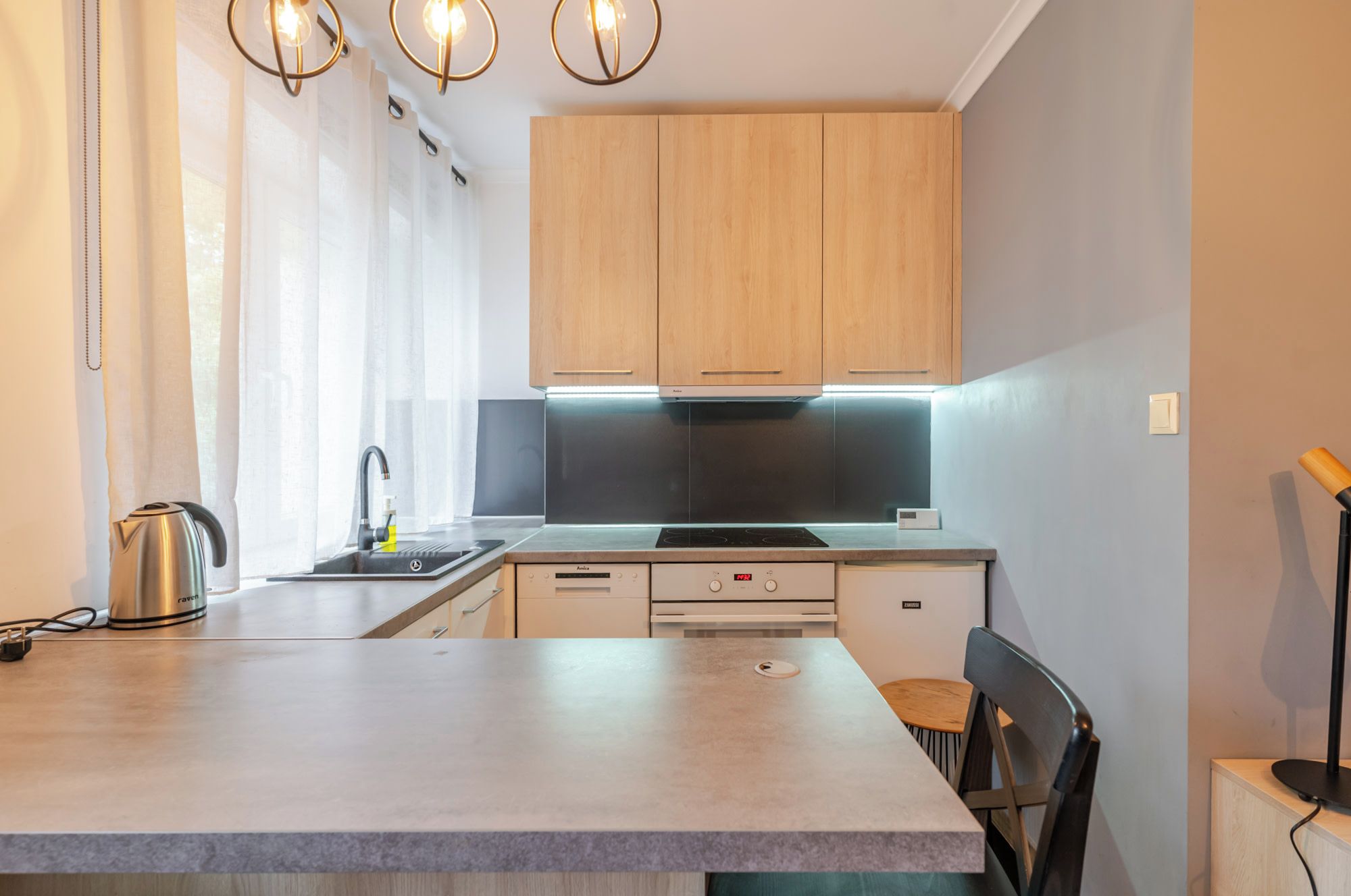 Una cocina moderna con armarios de madera, horno empotrado y hervidor de acero inoxidable.