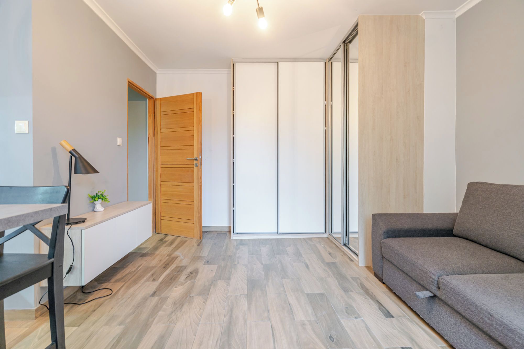 Una sala de estar moderna con un sofá gris, una puerta de madera y un escritorio con una lámpara.