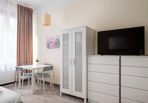 Ein Hotelzimmer mit einem Bett, einem Esstisch mit Stühlen, einem Fernseher auf einem Schrank und einem Fenster mit Vorhängen.