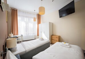 Ett hotellrum med två sängar, ett skrivbord, en stol, en tv som är monterad på väggen och ett träskåp.