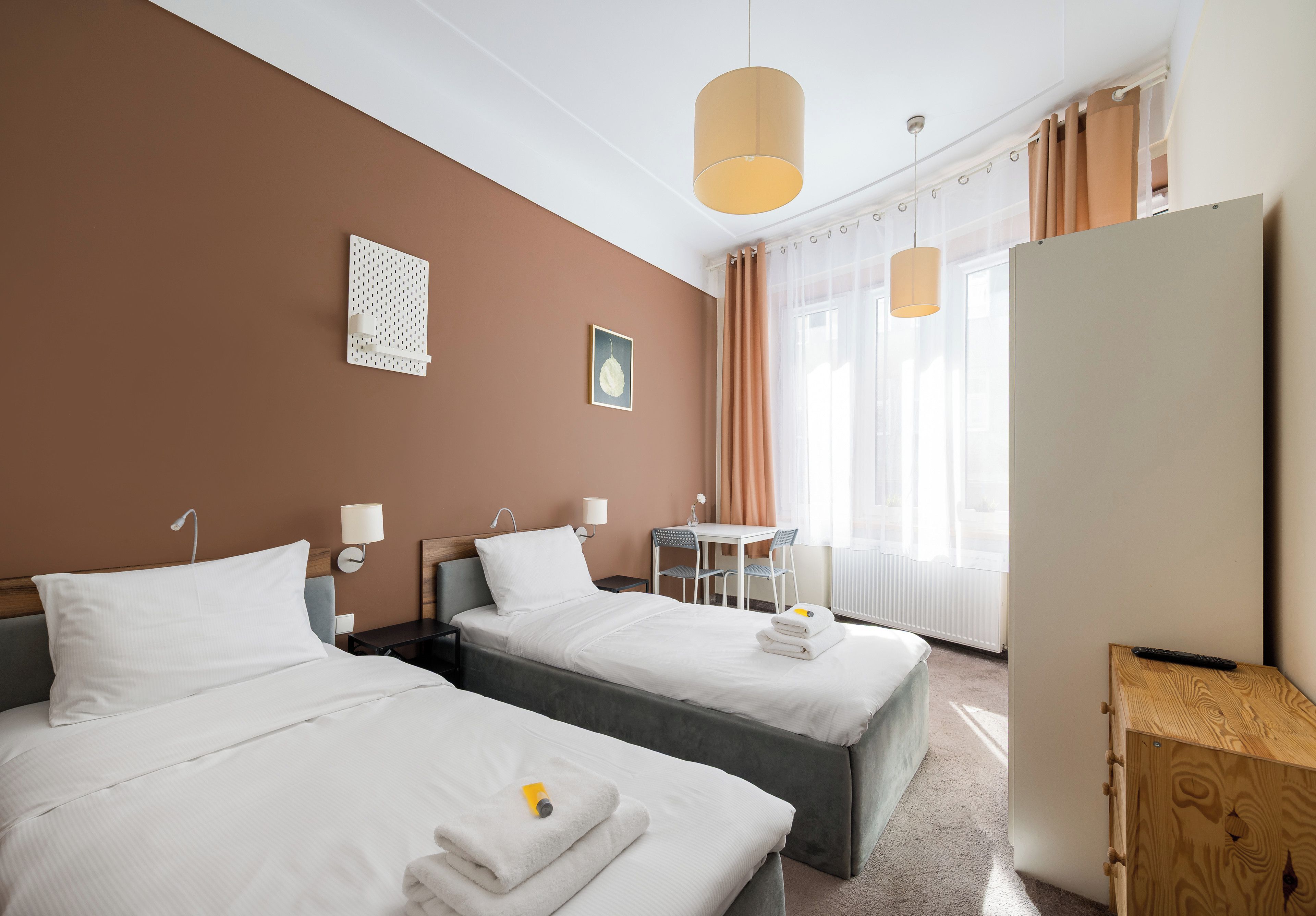 Een hotelkamer met twee bedden, een bureau, een stoel, een raam met gordijnen en een wandlamp.