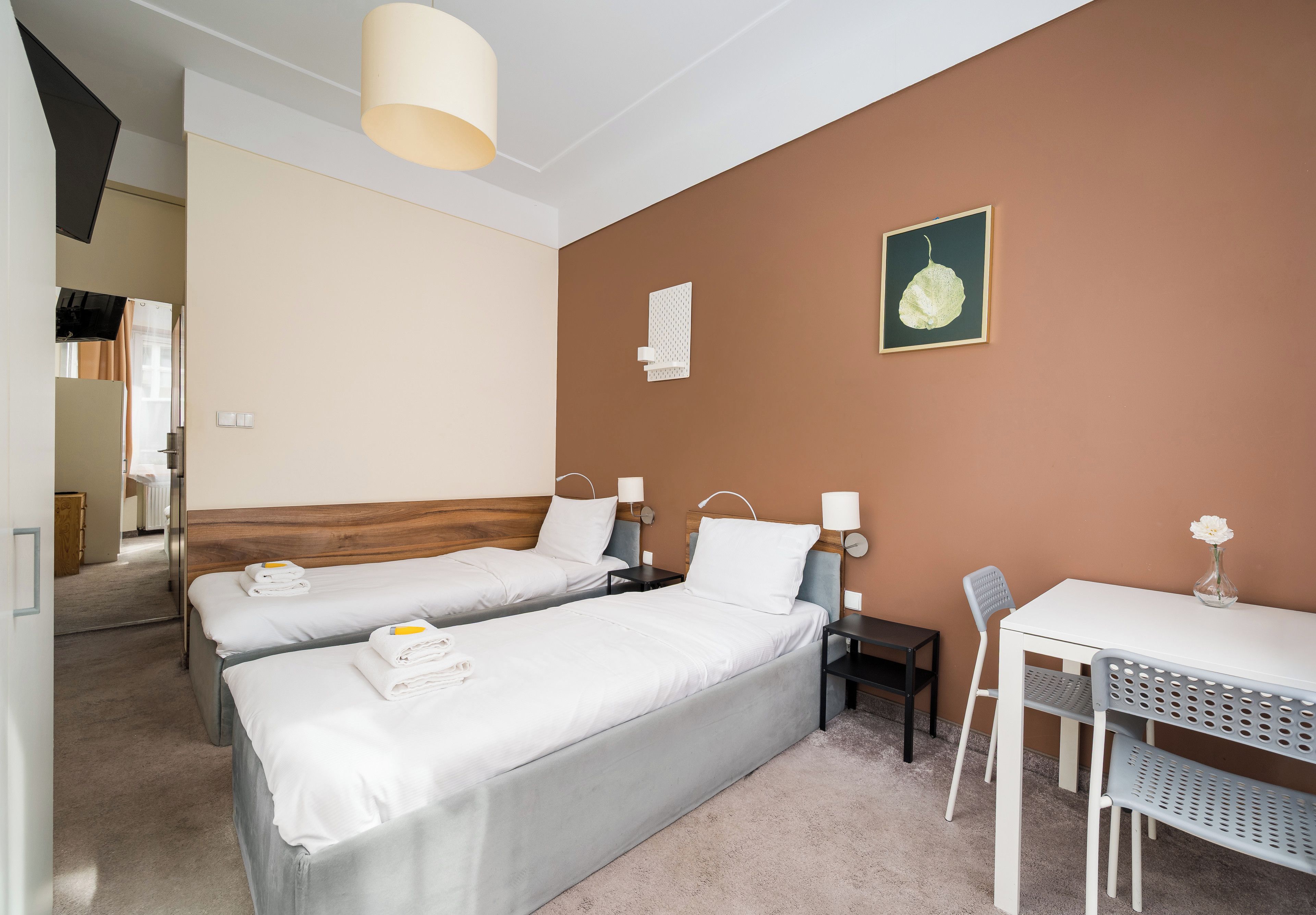 Habitación de hotel con dos camas, un escritorio, una silla, una mesa, una lámpara, un cuadro en la pared y un baño a la vista.