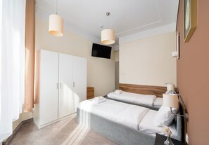 A hotel room with a bed, bedside tables, a TV, and a wardrobe.
