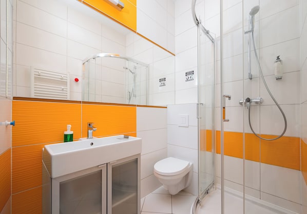 A modern bathroom with a glass-enclosed shower, a white sink with a soap dispenser, and a toilet.