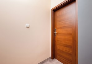 A wooden door with a handle and a small light switch on the wall.
