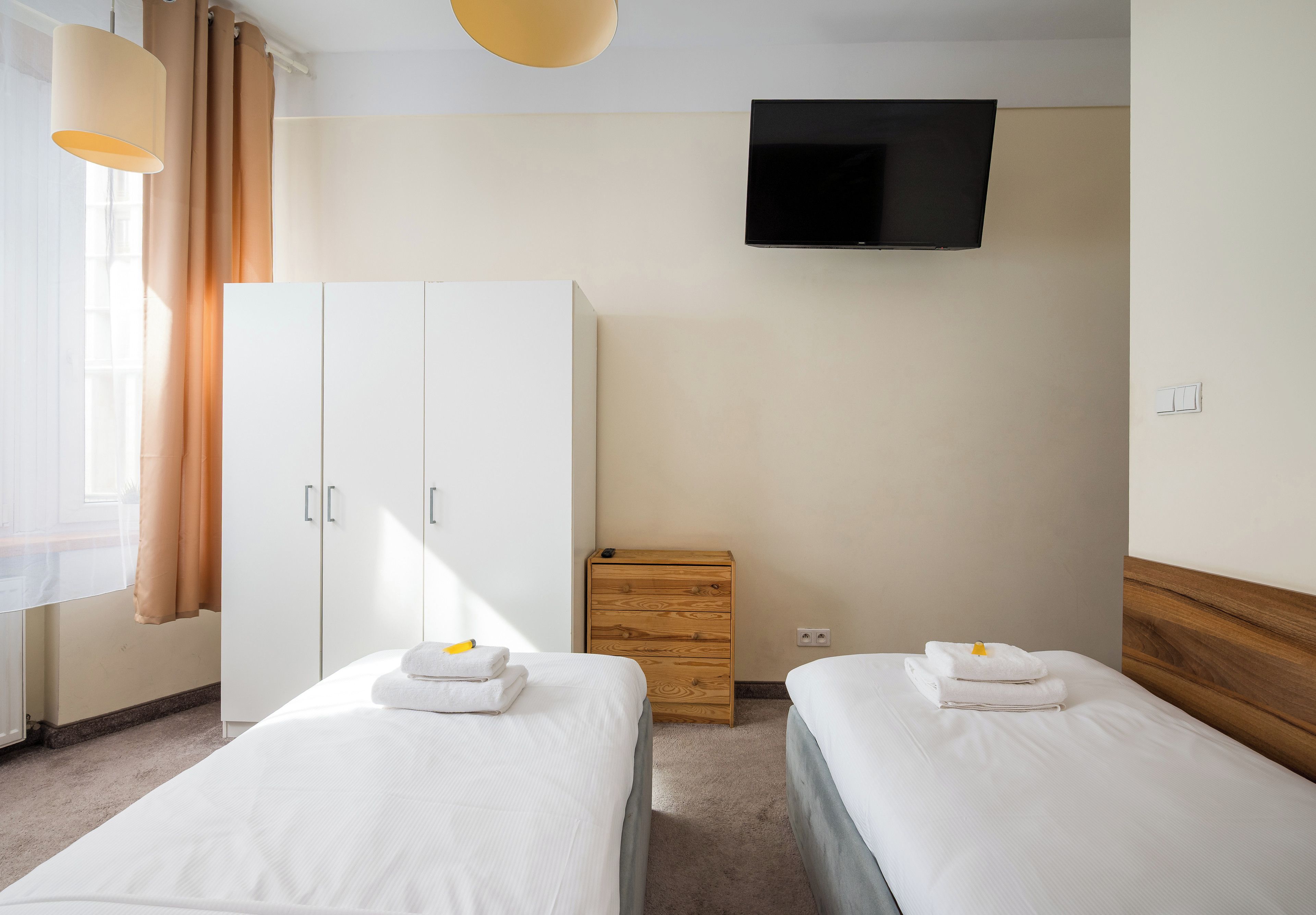 Una habitación de hotel con dos camas, un televisor montado en la pared y un armario.