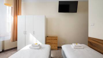 Una habitación de hotel con dos camas, un televisor montado en la pared y un armario.