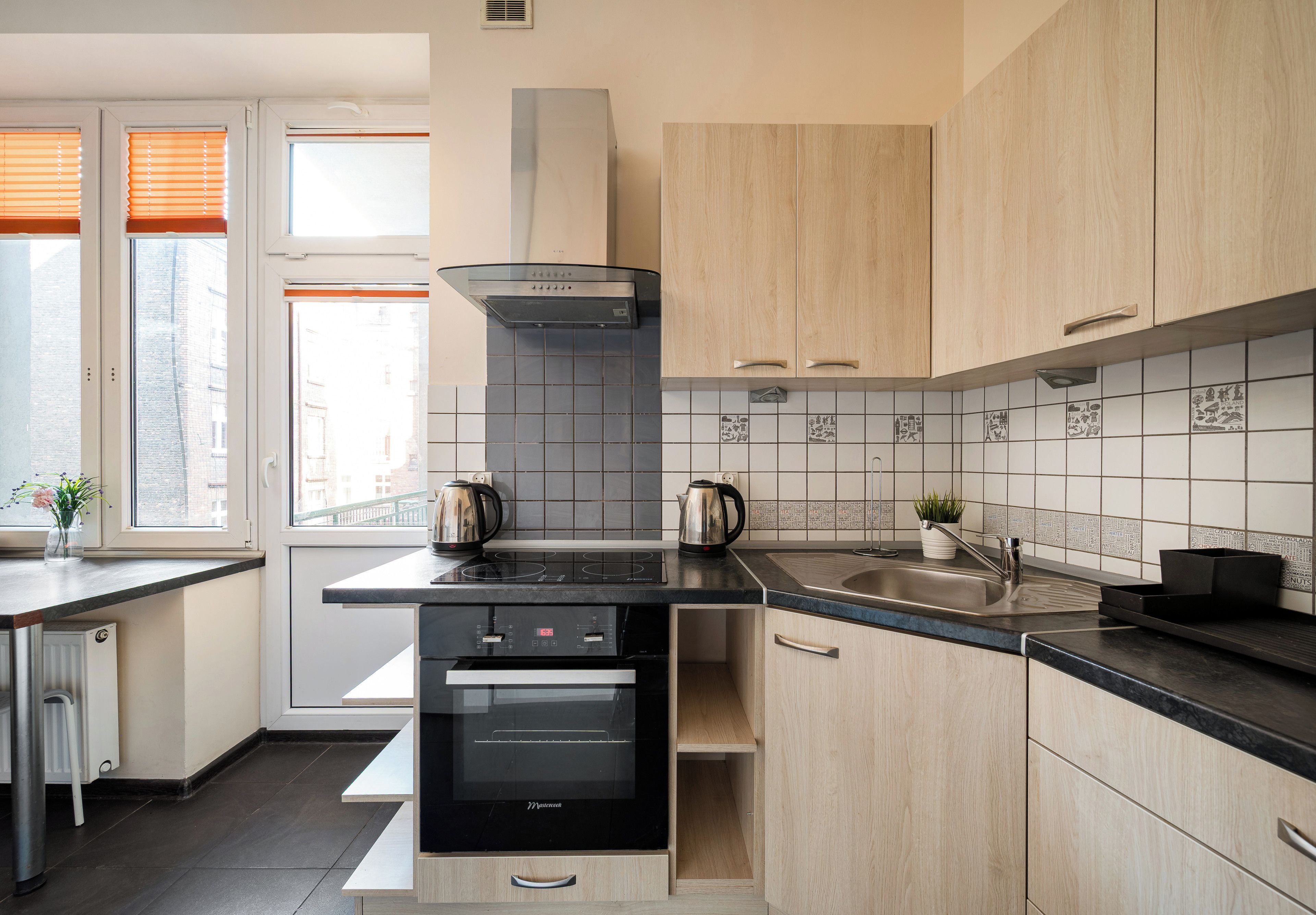 A modern kitchen with a black induction cooktop, a stainless steel sink, and wooden cabinets.
