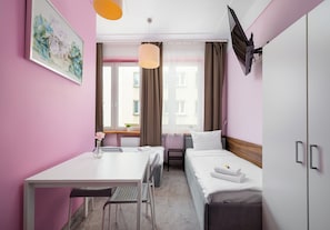 A hotel room with a bed, a desk, a chair, a bedside table, and a window with curtains.