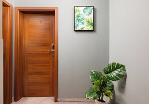 Una puerta de madera con el número 5, un cuadro enmarcado en la pared y una planta en maceta con hojas grandes.
