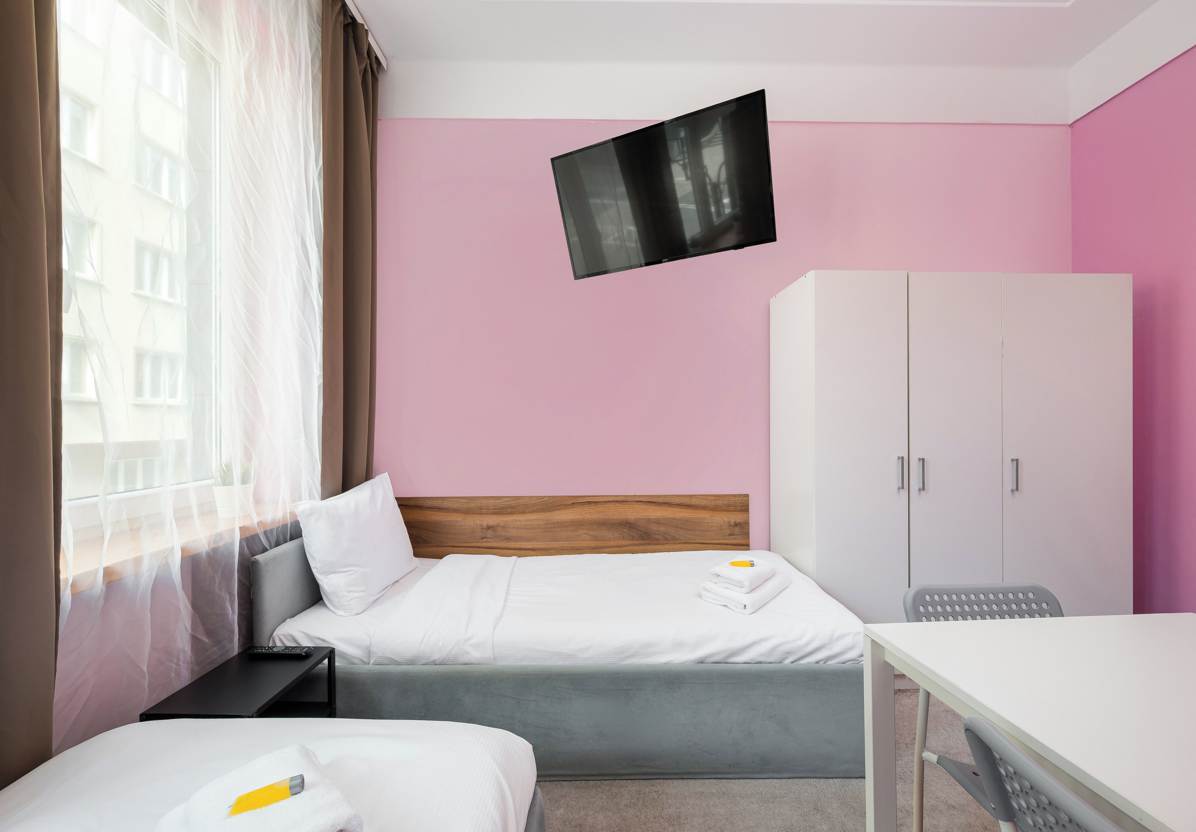 Habitación de hotel con cama, escritorio, armario y televisor fijado a la pared.