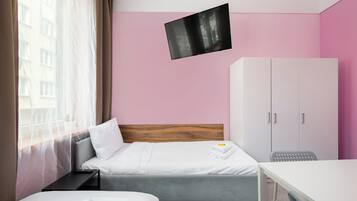 Habitación de hotel con cama, escritorio, armario y televisor fijado a la pared.