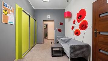 Un pasillo con una puerta verde, un reloj de pared, una cama con cubrecama acolchado y una lámpara roja.