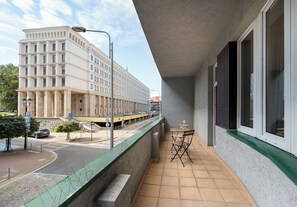 Ein Balkon mit Blick auf ein Gebäude, ein Tisch mit Stühlen und eine Straße mit Autos.