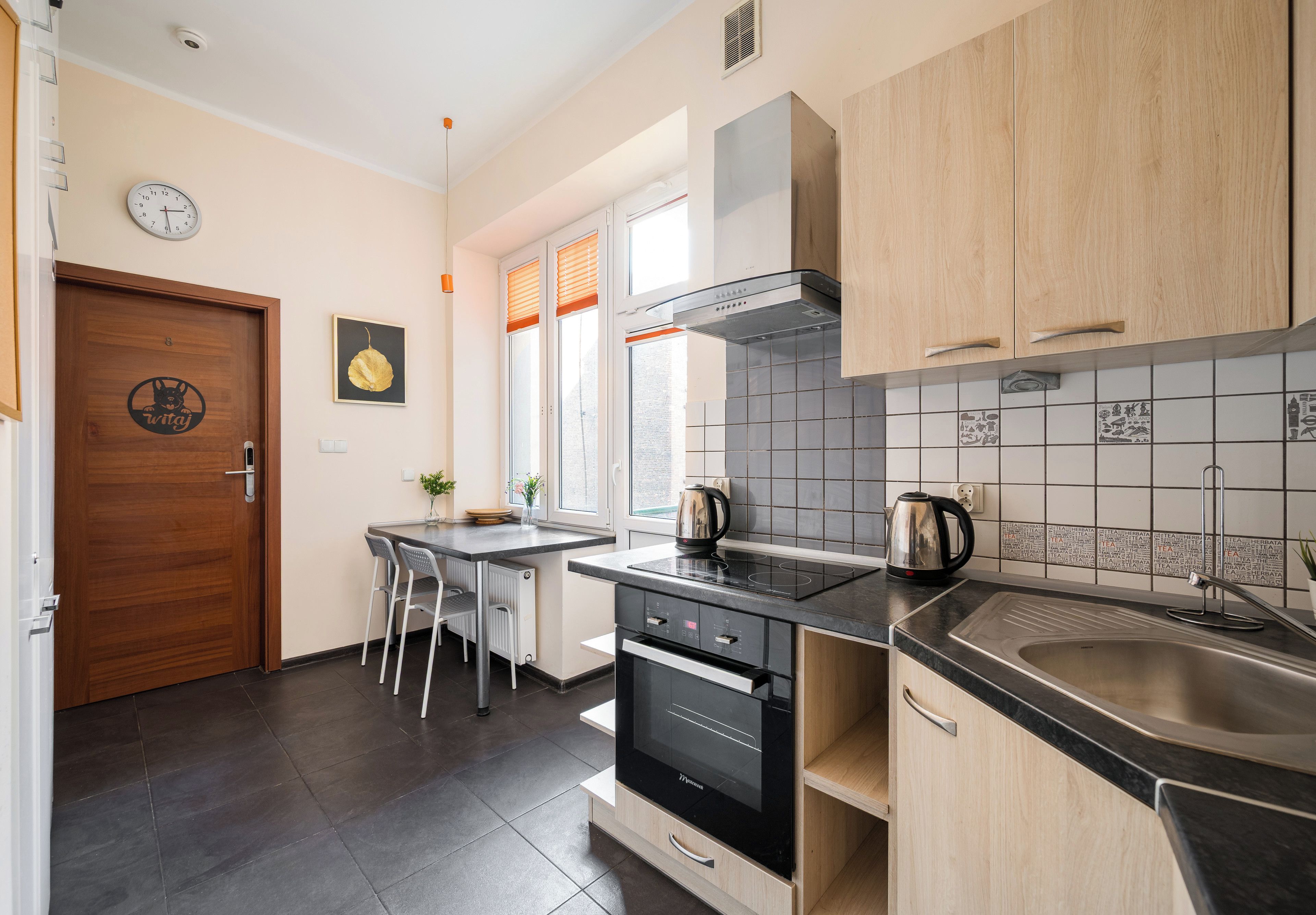 A modern kitchen with a black induction cooktop, stainless steel appliances, and wooden cabinets.