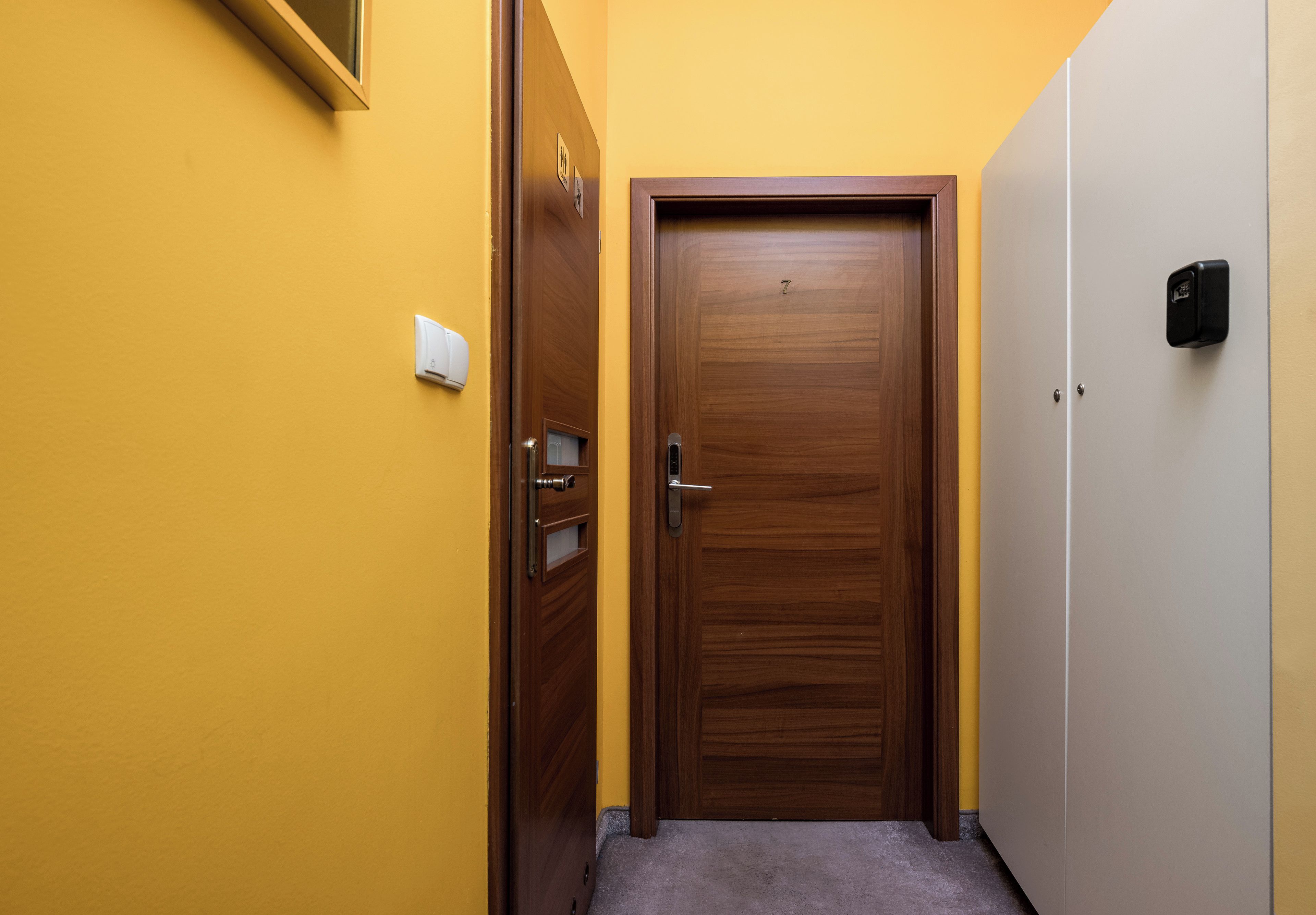 Un pasillo con una puerta de madera, un interruptor de luz y un timbre.