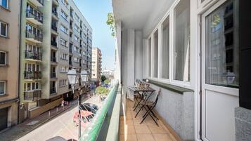 Een balkon met uitzicht op een straat, een tafel met stoelen en een hangplant.
