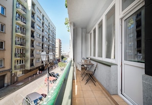 A balcony with a view of a street, a table with chairs, and a hanging plant.