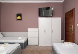 A bedroom with two beds, a wardrobe, a television, and a framed picture on the wall.