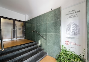 A staircase with a metal handrail leading to a room with a green speckled wall and a poster advertising a hostel.