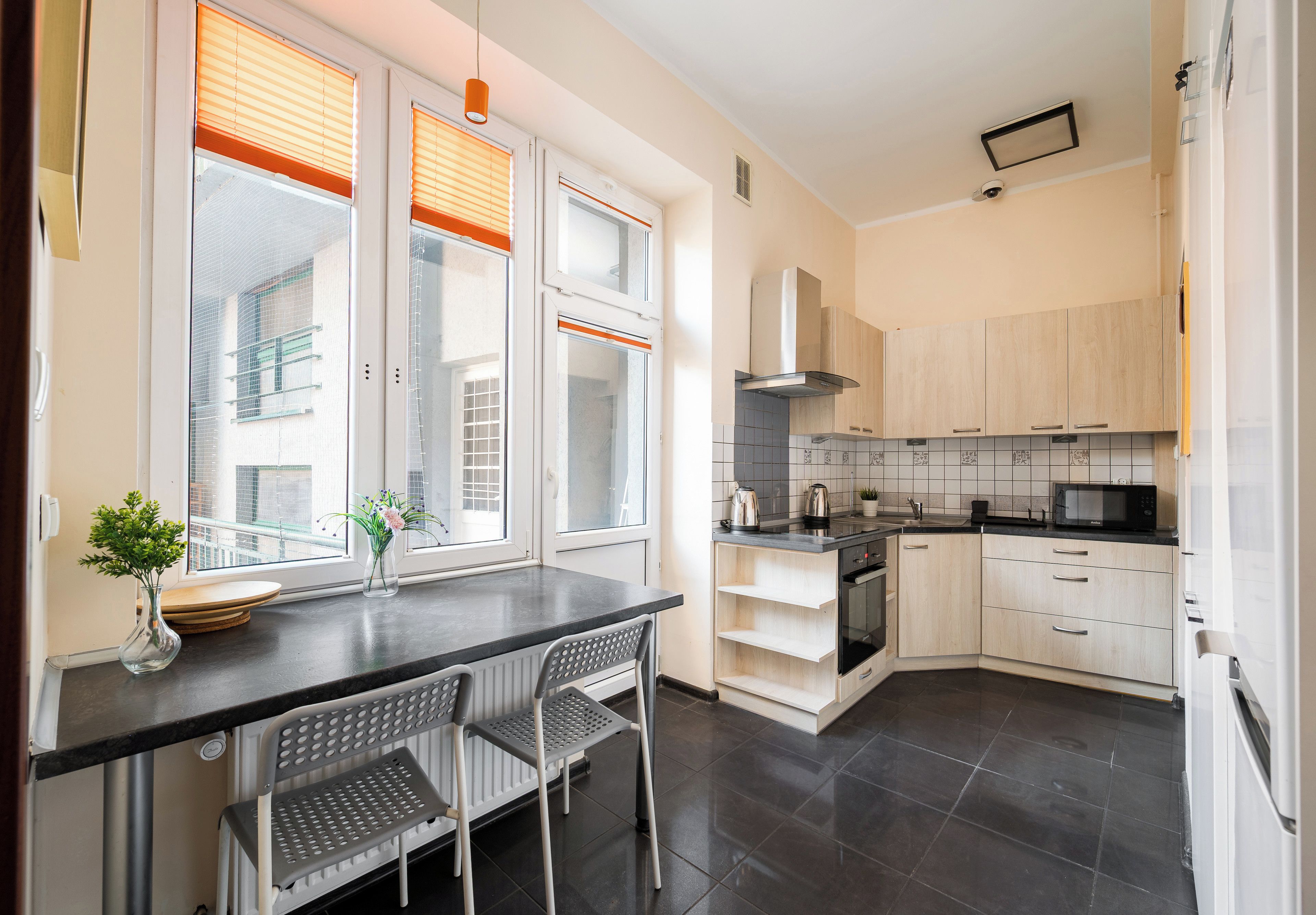 A modern kitchen with a dining area, featuring a built-in oven, microwave, and a large window with blinds.