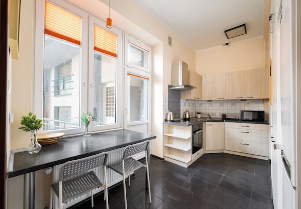 A modern kitchen with a dining area, featuring a built-in oven, microwave, and a large window with blinds.