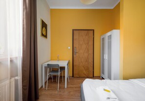 Ein Zimmer mit einem Bett, einem Schreibtisch mit Stuhl, einem Kleiderschrank und einer Tür.