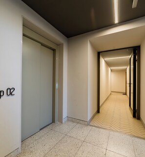 Un couloir au sol carrelé, une porte portant l’inscription « 02 », et un passage menant à une autre pièce.