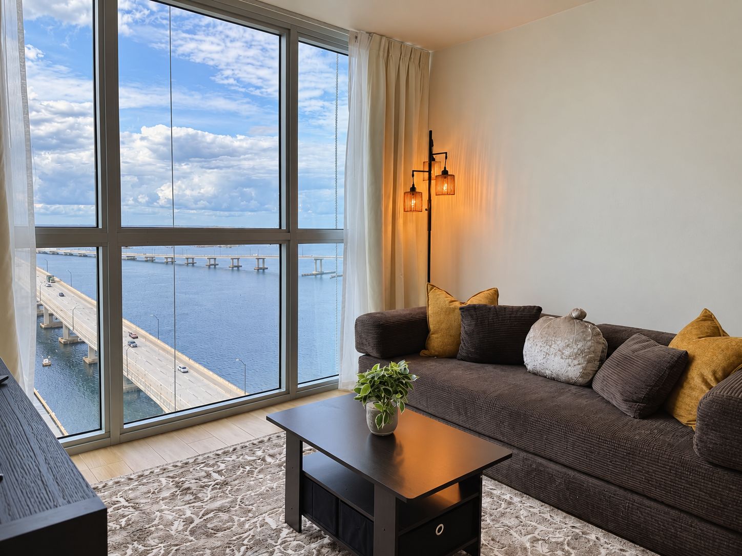 A modern living room with a large window, a sofa, a coffee table, and a lamp.