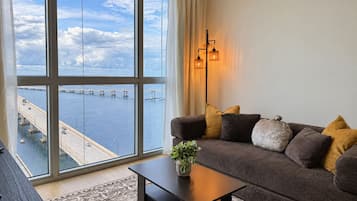 A modern living room with a large window, a sofa, a coffee table, and a lamp.
